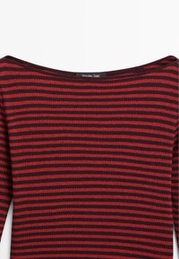 Ribbed long-sleeve top in deep red and dark burgundy stripes. Wide scooped neckline, soft texture, and minimalist design. Brand label visible.