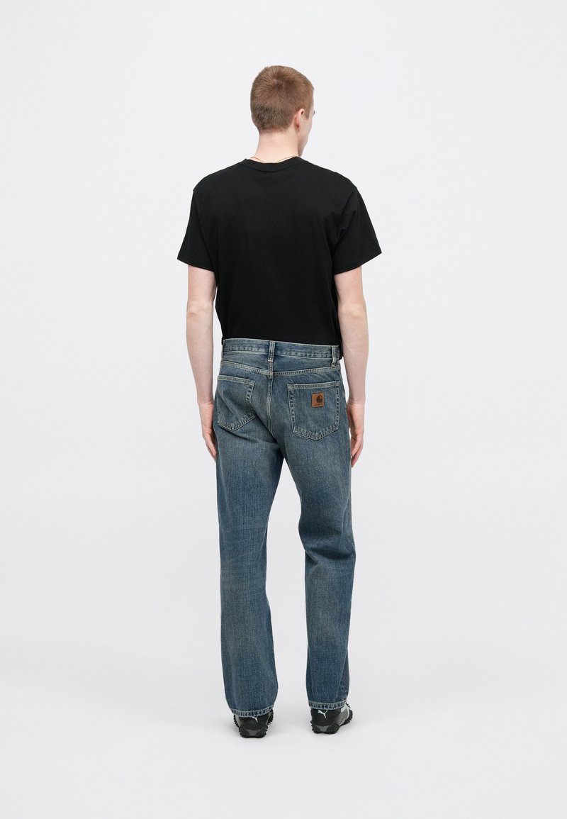 Black short-sleeve t-shirt paired with loose-fit blue denim jeans featuring a brand patch on the back pocket and a frayed hem.