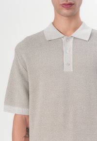 Kortermet polo-skjorte i lys beige, med strukturvev, krage og tre knapper på pløstret.