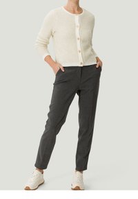 Kremowy krótki kardigan o miękkiej fakturze i okrągłym dekolcie, ozdobiony jasnobrązowymi guzikami. Szare dopasowane spodnie o slim fit z kieszeniami.