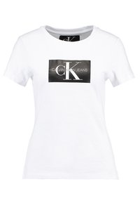Camiseta de algodón blanca con mangas cortas, cuello redondo, que presenta un logotipo rectangular negro con "CALVIN KLEIN JEANS" y "CK" en texto blanco.