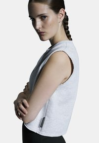 Heledad hall grey ilma varrukatega topp, millel on toored servad ja tekstuuriga kangas, sisaldades külgtagi. Modell poseerib käed ristatud valge taustal.