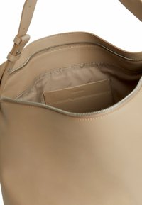 Beige leren schoudertas met een gladde textuur, voorzien van een ritssluiting, binnenzak en subtiele branding op de voering.