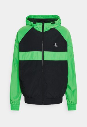 Zwart en felgroen windjack met capuchon, voorrits en CK-logo op de borst, elastische manchetten en een groene horizontale streep over de voorkant.