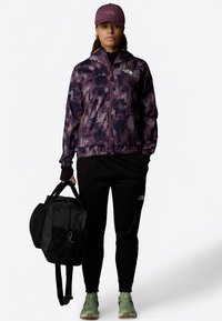 Violetti maastokuvioinen takki, mustat housut ja vihreät kengät; kantaa mustaa duffel-laukku. Ominaisuuksiin kuuluvat vetoketjut, joustavat hihansuut ja merkkilogot.