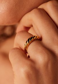 Gouden ring met een gedraaid ontwerp, voorzien van een gepolijste afwerking en gladde, ronde randen, gedragen op een vinger tegen een lichte huid.