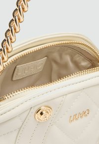 Gep quiltete weiße Handtasche mit goldenen Beschlägen, ausgestattet mit einem metallischen Logo und einem goldenen Kettenriemen. Gefüttertes Innenfach mit Reißverschluss.