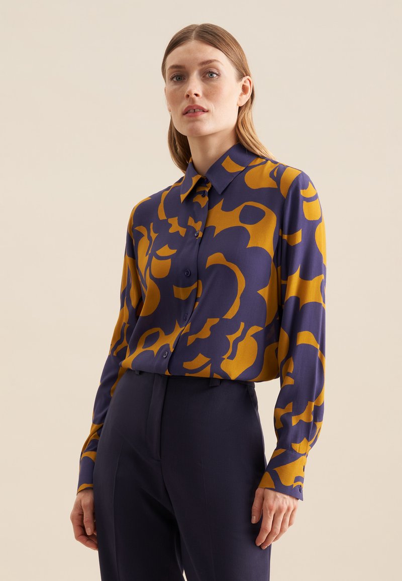 Lange mouw overhemd in marineblauw en mosterd met abstract patroon, knoopsluiting aan de voorkant en een klassieke kraag. Lichtgewicht stof met een soepele textuur.