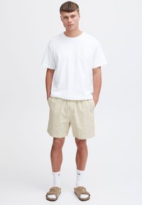 White cotton T-shirt, beige shorts, white ankle socks, and brown sandals. Simple design, relaxed fit, and neutral colors.