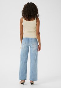 Débardeur côtelé beige clair associé à un jean en denim clair à taille haute et jambes larges, poches arrière visibles et sandales à talons simples.