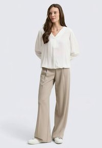 Voľne strihaná biela blúzka s véčkovým výstrihom a dlhými rukávmi, doplnená béžovými širokými nohavicami a bielymi teniskami. Minimalistický dizajn.