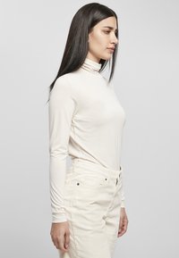 Maglione a collo alto di colore crema, dal design aderente e texture morbida. Abbinato a pantaloni di velluto a coste bianchi, con vita alta e tasche.