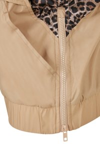 Beżowa lekka kurtka z zapięciem na zamek błyskawiczny, wyściełana podszewką w panterkę i z marszczonym, elastycznym dołem. Gładka, wodoodporna tkanina.