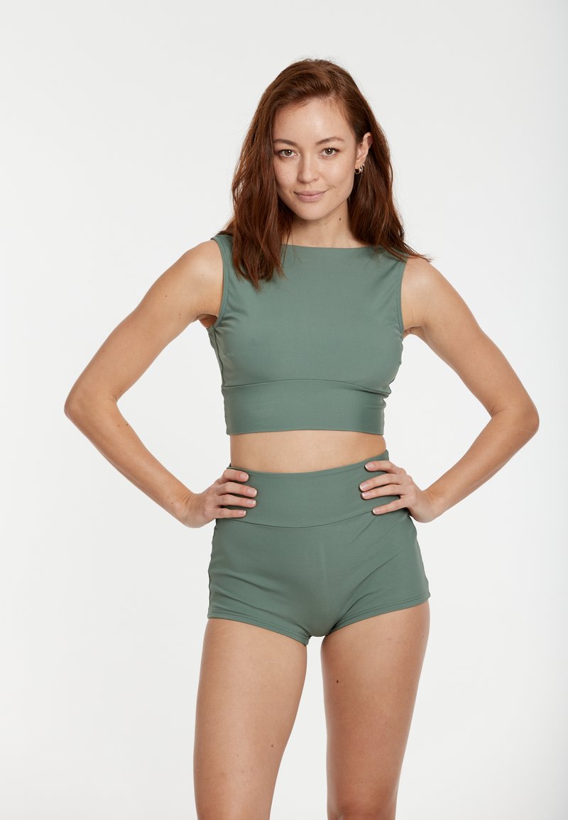 Bra sportivo verde a costine con spalline larghe abbinato a pantaloni corti a vita alta. Entrambi realizzati in un tessuto liscio ed elastico.
