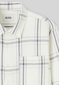 Chemise à carreaux blancs avec des lignes de grille violet clair, col boutonné, tissu texturé et poche poitrine. Étiquette de marque visible.