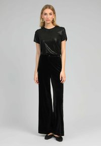 Haut noir à manches courtes avec une finition brillante, associé à un pantalon large en velours noir taille haute et des chaussures plates noires.