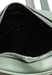 Borsa in pelle verde menta con apertura con cerniera, che mostra un interno in tessuto nero e accessori in argento lungo la cerniera.