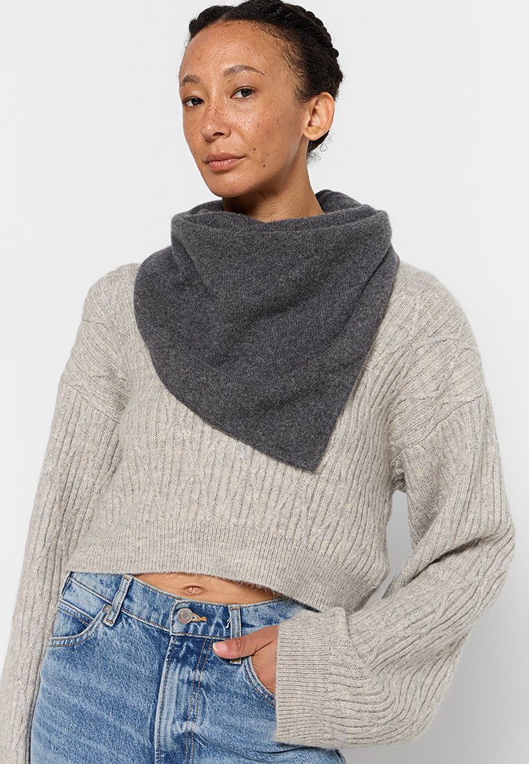 Grau wollener Schal in dreieckiger Form, der um den Hals drapiert ist, getragen über einem hellbeigen gestrickten Pullover. Strukturierter Stoff mit einem gemütlichen Erscheinungsbild.