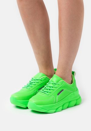 Baskets athlétiques vert fluo avec une tige lisse en synthétique, un laçage et une semelle épaisse et texturée présentant un design en vagues.