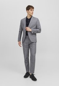 Completo in lino grigio con una vestibilità slim, caratterizzato da un blazer con rever a notched e pantaloni abbinati, abbinato a una polo scura e scarpe nere.