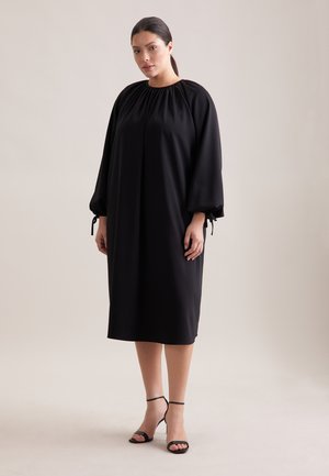 Schwarzes Kleid mit Ballonärmeln und hohem Ausschnitt, mit gerafften Details und Bändern an den Manschetten. Glatter Stoff, knielange Silhouette.