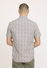 Chemise à manches courtes en tissu léger avec une base blanche, présentant un motif floral coloré en rose et vert, avec un col standard et un empiècement au dos.