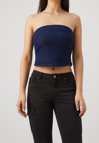 Marine strapless denim crop top met een aansluitend ontwerp. Gecombineerd met zwarte cargobroeken met zijzakken en een knoopsluiting.