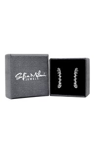 Orecchini in argento con un design unico simile a ossa, esposti all'interno di una scatola di velluto nero, con un esterno grigio testurizzato e logo.