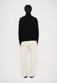 Čierny rolák so voľným strihom, vyrobený z jemnej tkaniny. Skombinovaný s krémovými nohavicami s širokým strihom a čiernymi topánkami.