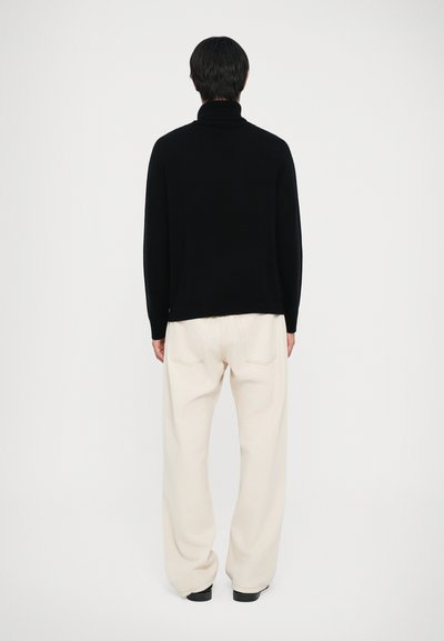 Maglione a collo alto nero con vestibilità comoda, realizzato in tessuto morbido. Abbinato a pantaloni larghi color crema e scarpe nere.