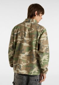 Tarnjacke in beige, grünen und braunen Stoffen. Mit Kragen, elastischen Bündchen und lockerer Passform. Dezente Textur- und Musterdetails.