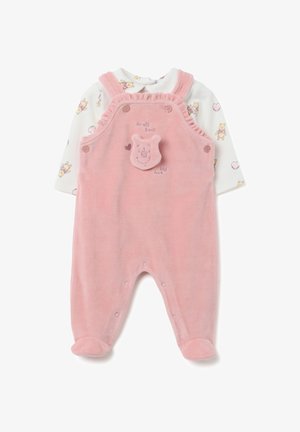 Une barboteuse rose pour bébé avec des pieds, portée sur une chemise à manches longues blanche ornée de petits ours en dessin animé et de cœurs, décorée d'un visage d'ours et de texte sur le devant.