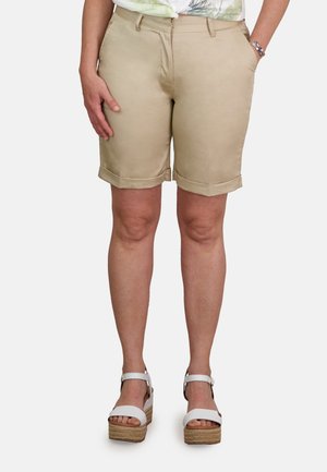 Pantalones cortos de color beige claro con puños enrollados, bolsillos frontales y lazos para cinturón, combinados con sandalias de plataforma blancas con tiras en el tobillo.