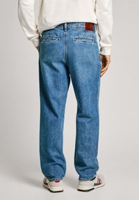 Blå denimjeans med en avslappnad passform, med en läderpatch på baksidan av midjan, två bakfickor och en blekt yta.
