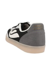 Black and gray sneaker with a textured fabric upper, white accents, and a beige rubber sole. Features gold branding on the heel.