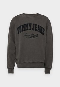 Grijze sweatshirt met een ronde hals en ribgebreide manchetten. Heeft een groot, fluwelen zwart logo met de tekst "TOMMY JEANS New York" op de voorkant.