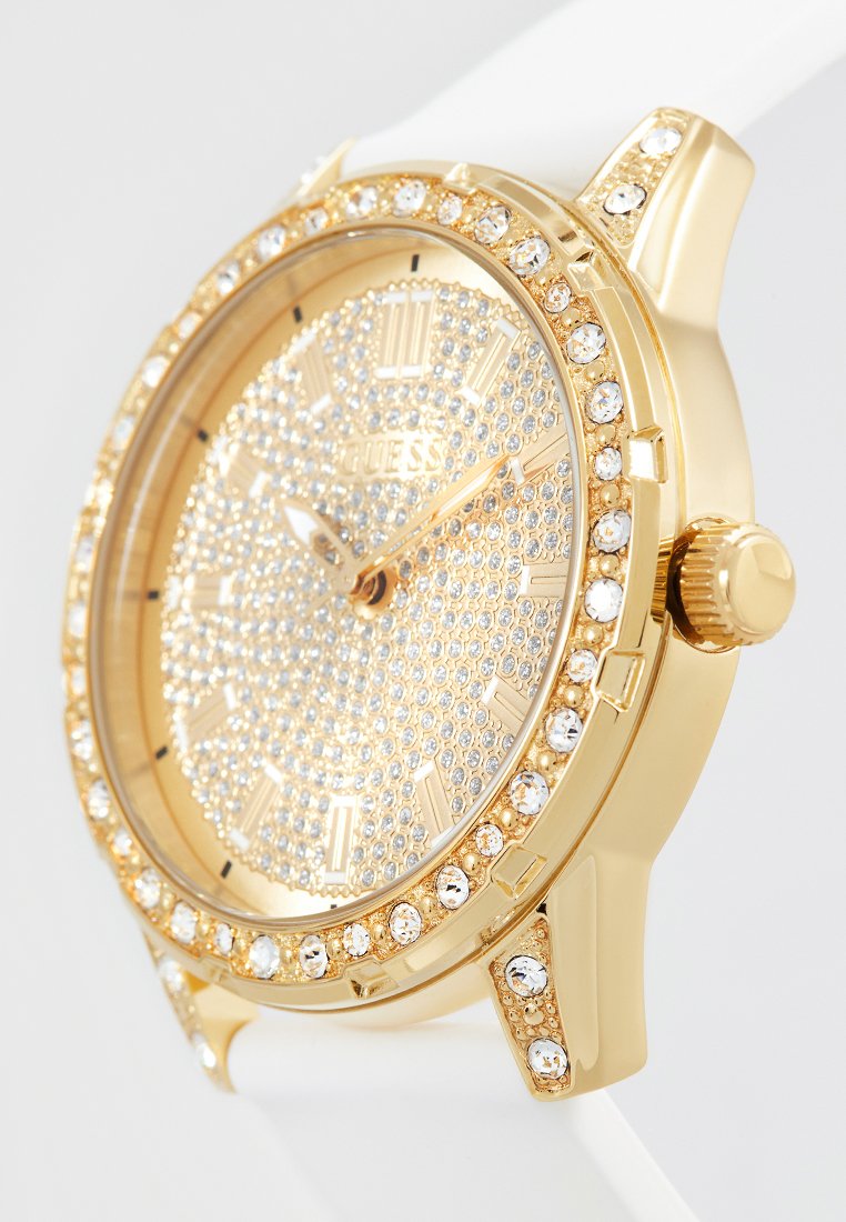 Montre-bracelet dorée avec cadran et lunette ornés de cristaux, index en chiffres romains et bracelet blanc, affichant l'heure à 10h10.