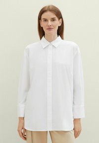 Chemise blanche à manches longues avec un col classique et une coupe droite, fabriquée en tissu lisse avec un minimum de détails.