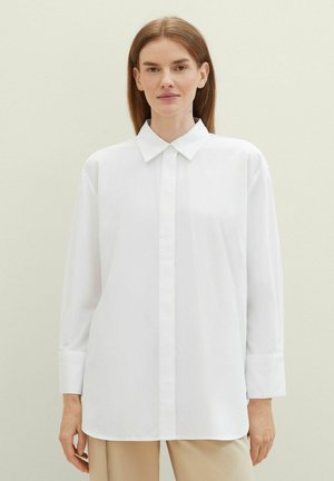 Chemise blanche à manches longues avec un col classique et une coupe droite, fabriquée en tissu lisse avec un minimum de détails.