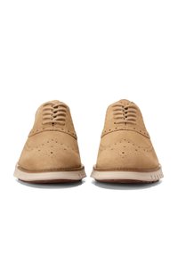 Světlé semišové oxfordky s brogue detaily, s kulatou špičkou, šesti dírkami na tkaničky a bílou gumovou podešví s texturou.