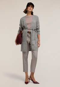 Szary dzianinowy kardigan z paskiem, jasnopurpurowy top, szare spodnie w prążki i burgundowa torebka. Całość dopełniają wąskie obcasy.