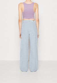 Ljusblå kordflodbyxor med vida ben, två bakfickor och en etikett på midjebandet. I kombination med en ljuslila kort tanktopp.