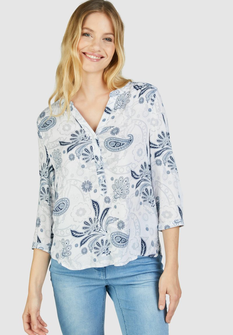 Weiße Bluse mit blauen Paisley- und Blumenmustern, mit V-Ausschnitt und dreiviertel Ärmeln. Leichter Stoff mit lockerer Passform.