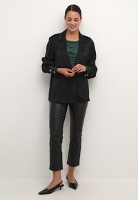 Blazer negru cu o croială lejeră, guler mare și manșete cu butoane peste un top cu dungi verzi. Asortat cu pantaloni din piele negri și pantofi slingback ascuțiți.
