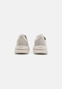 Light gray athletic shoes with a textured mesh upper and soft rubber sole, featuring a pull tab and smooth accents on the heel.