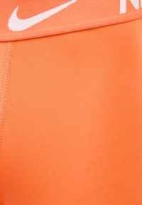 Close-up van oranje Nike sportstof met zichtbare naden en gedeeltelijk wit Nike-logo op de tailleband.