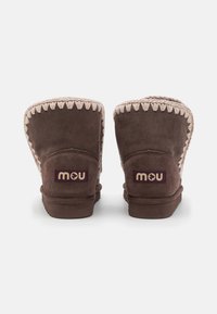 Stivaletti in suede marrone con una fodera in pile beige, caratterizzati da cuciture a contrasto e un logo in tessuto viola sul retro.