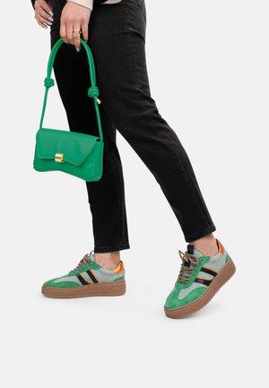 Baskets en suède vert et gris avec des rayures noires et des accents orange. Assorties à un jean noir et un sac à main vert.