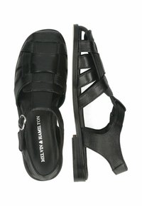 Czarne skórzane sandały z zamkniętym noskiem, odkrytymi piętami i zapięciem na klamrę. Posiadają plecione paski i niski obcas w kształcie bloku.