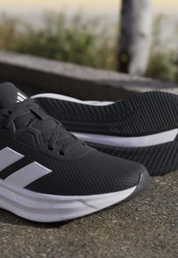 Paire de chaussures de course athlétiques noires et blanches reposant sur une surface en béton à l'extérieur avec un arrière-plan flou.